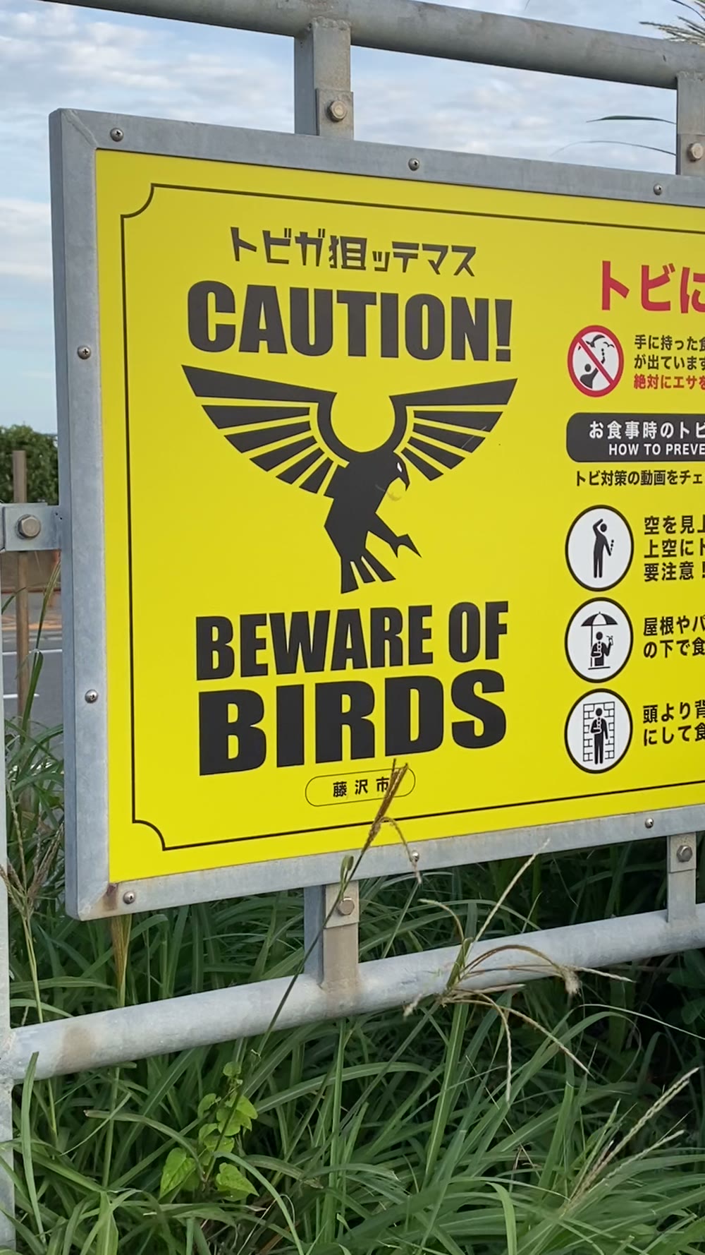 手に持った食べ物を狙う鳥に注意と書かれた藤沢市の看板