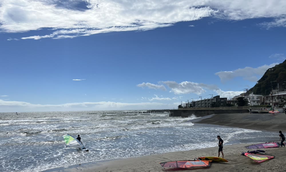 風が強い七里ヶ浜の海と、浜辺のウインドサーフィンの道具